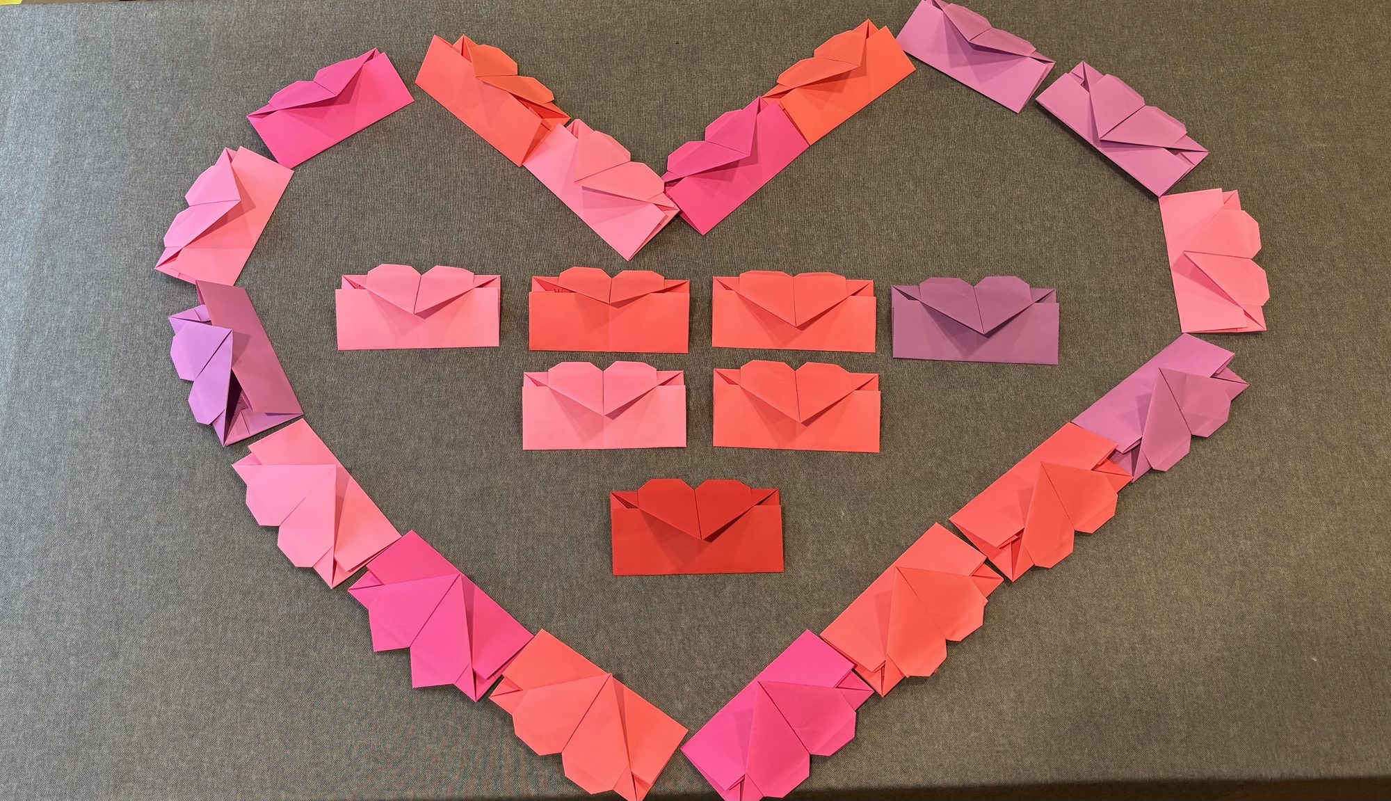 Folded heart envelopes in pinks and reds, stacked and ready to pack.