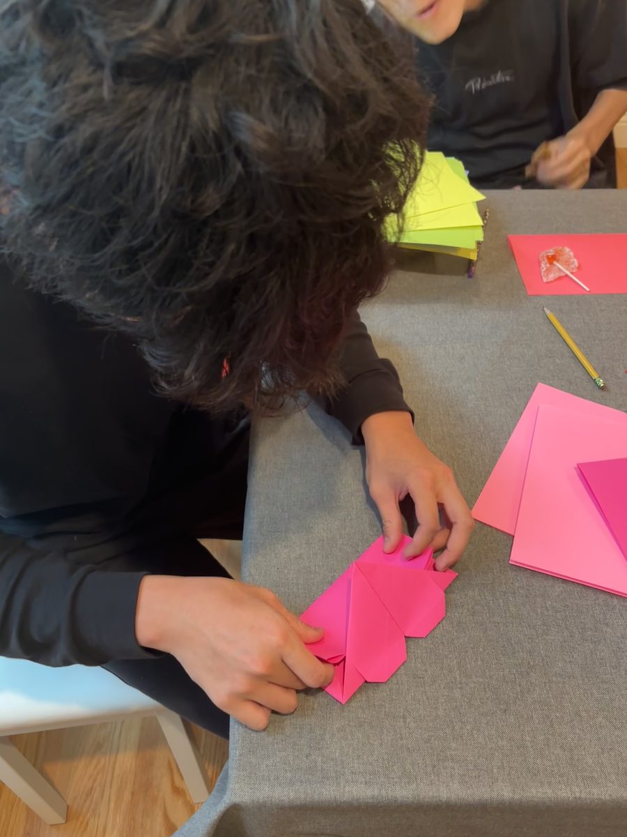 Close-up of hands creasing a hot-pink paper heart envelope.