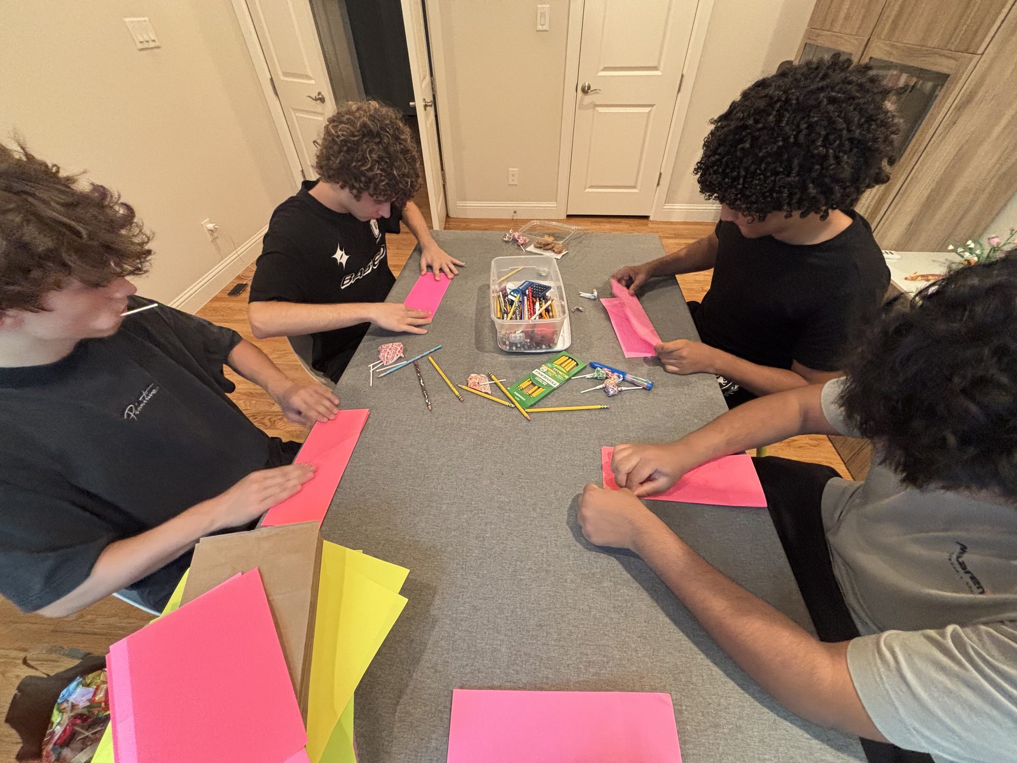 Overhead view of four teens starting their first folds at a grey table, with a pencil bin and candy between them.